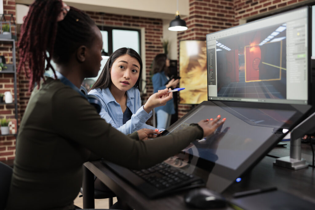 Two women collaborating in a digital studio using design software and a stylus tablet, illustrating AI in creative work